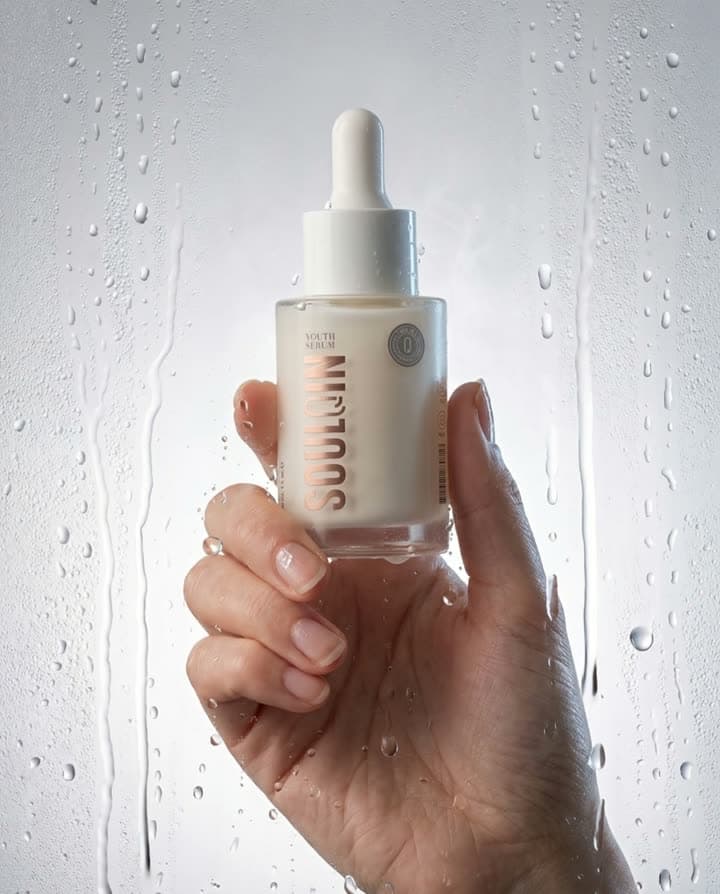 Islak cam önünde Soulqin serum şişesini tutan el